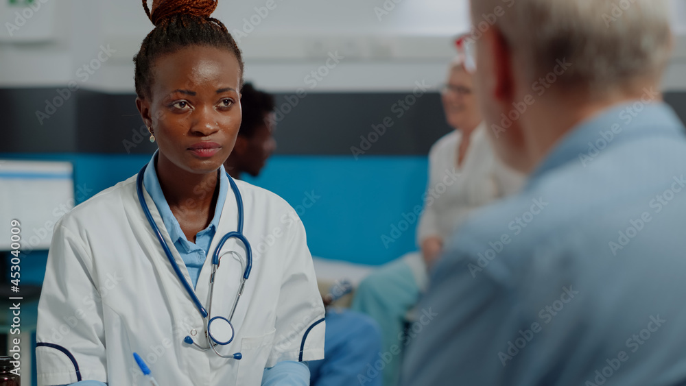 Close up of african american doctor doing consultation with senior patient sitting at desk in medical office. Black medic with white coat giving professional advice to elder man Close up of african american doctor doing consultation with senior patient sitting at desk in medical office. Black medic with white coat giving professional advice to elder man