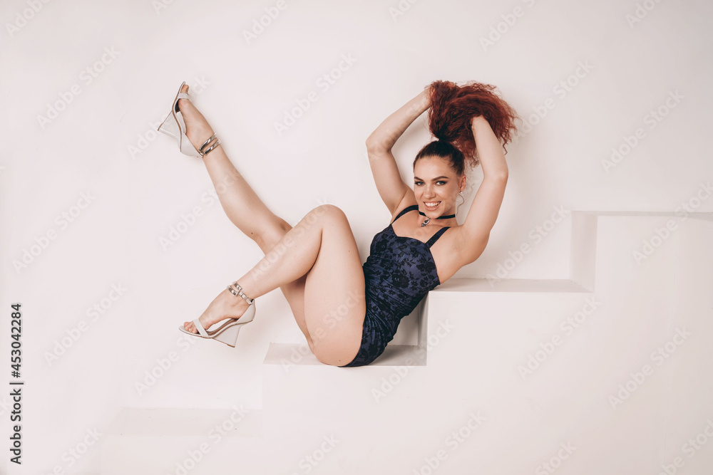 Beautiful and sexy girl with red hair. The girl flirts and smiles. The  dancer's long legs. The dancer poses for the camera. A girl in a blue dance  swimsuit. Stock Photo