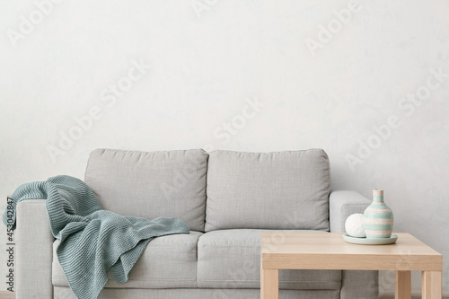 Sofa with plaid and table near light wall