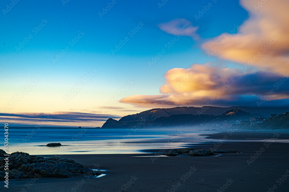 Obraz premium Sunset lights up the clouds over the cape in a long exposure image of the beach