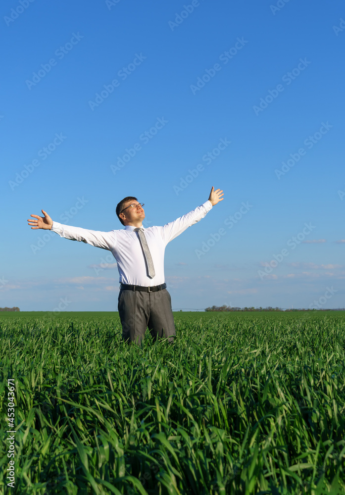 businessman poses in a field, he looks into the distance and rests, green grass and blue sky as background businessman poses in a field, he looks into the distance and rests, green grass and blue sky as background