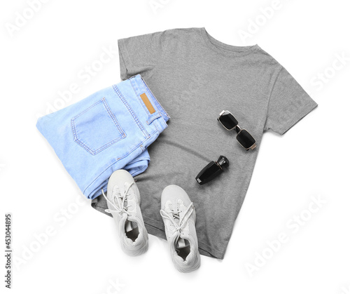 Stylish t-shirt, sunglasses, shoes, jeans and bottle of perfume on white background