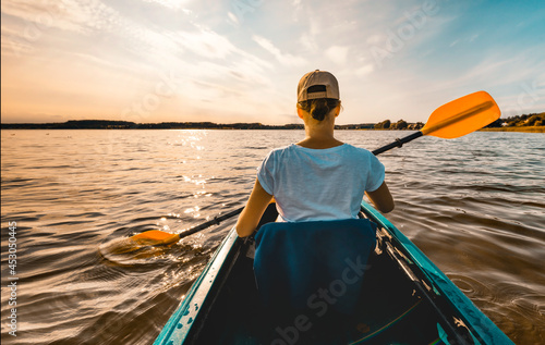 Young girl in a kayak paddling on the lake at sunset - view from behind her back