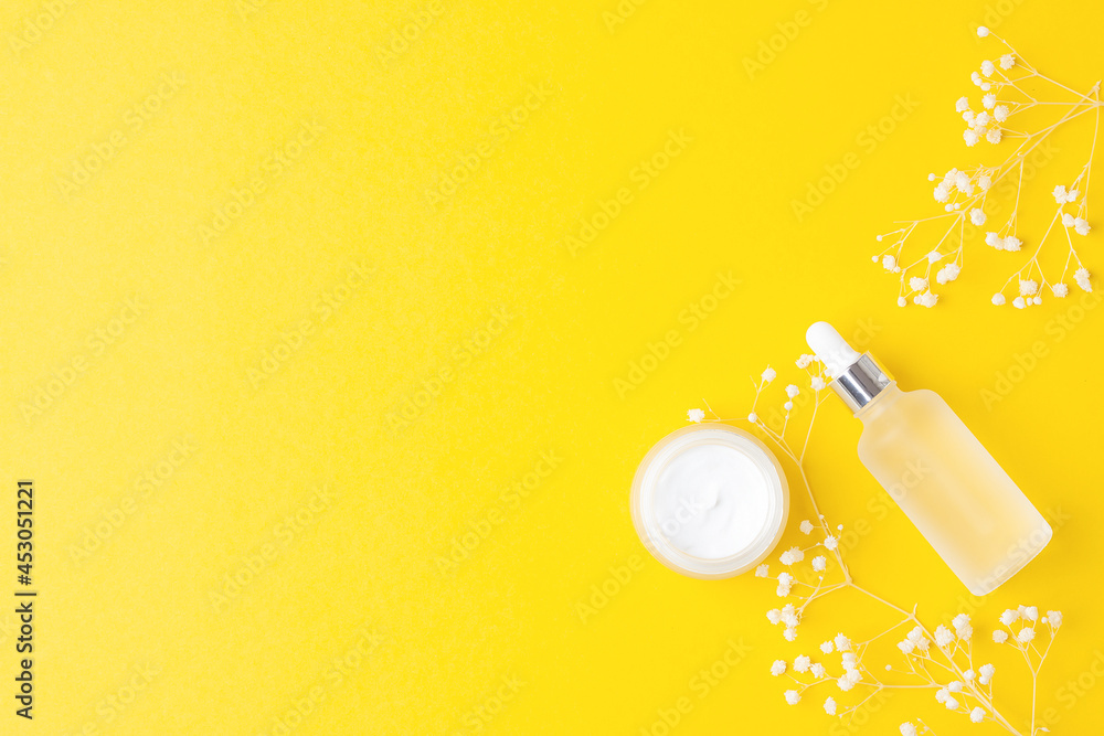 Cosmetic skin care products and flowers on yellow background. Flat lay, copy space