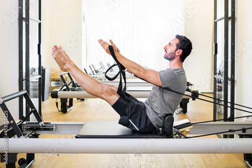 фотографія Fit muscular man doing a teaser pilates exercise on a reformer