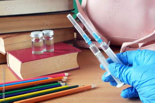 bottles and syringes of vaccine aganist covid-19 near book pile and school supplies, back to school in coronavrus time concept
