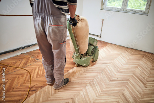 Repairman restoring parquet with a sanding machine.