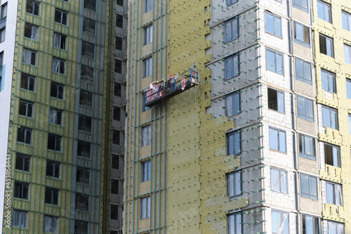 workers are insulating the wall of a building. Construction site. Foreign workers. Insulation panels. Hanging cradle. Hazardous work. Work on the street. Gray wal photo