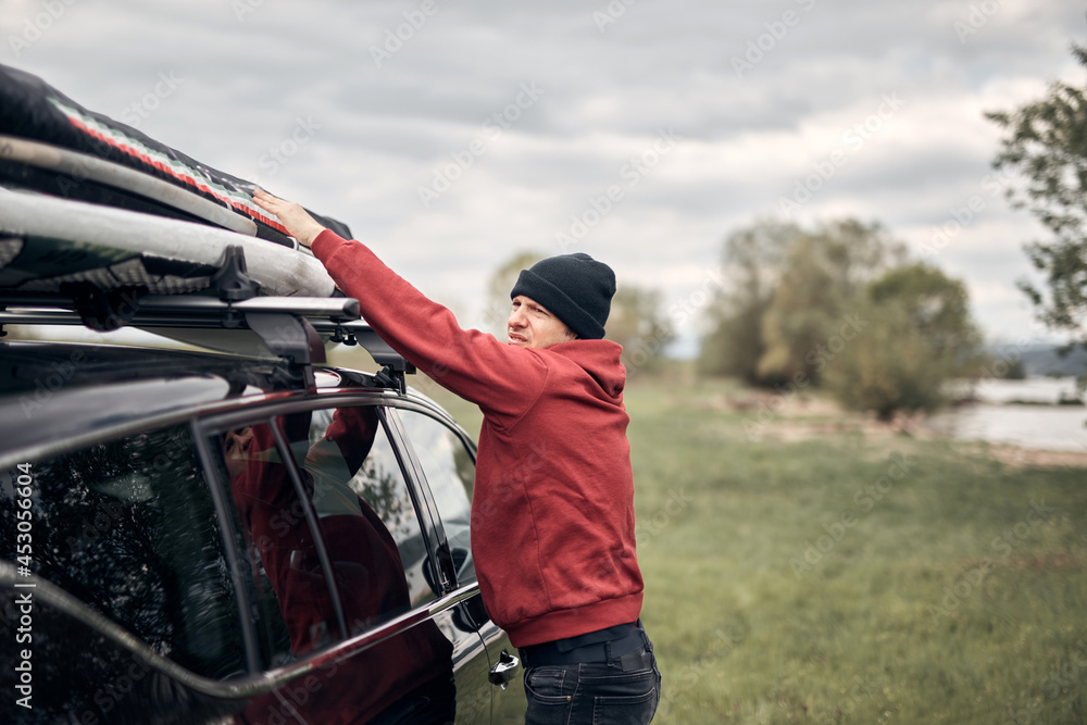 Obraz premium Windsurfer and camper packing and unpacking from a car's roof rack in nature.