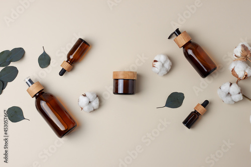 Cosmetic skin care products with flowers and eucalyptus on pastel beige background. Flat lay, copy space
