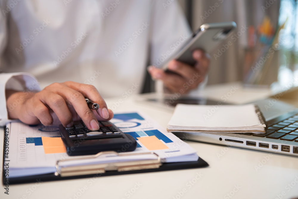 Close up male hand using calculator and smartphone calculate about cost at home office. Close up male hand using calculator and smartphone calculate about cost at home office.
