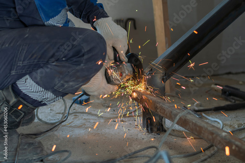 The cut off male hands of a worker use a grinder to clean a weld seam on a metal structure. Bright sparks of hot metal fly.