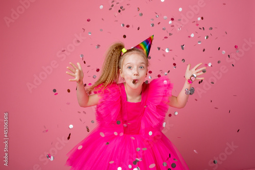 a little girl on a pink background blowing confetti celebrates her birthday
