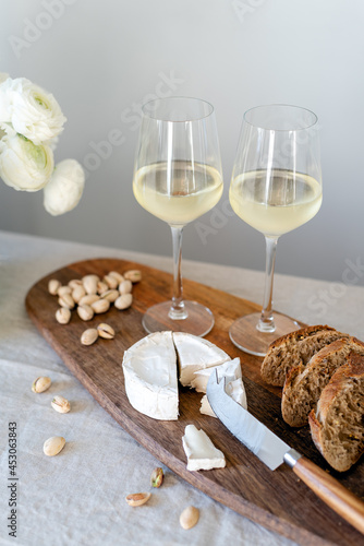 Two glasses of white wine and a wooden board with appetizers on the table.