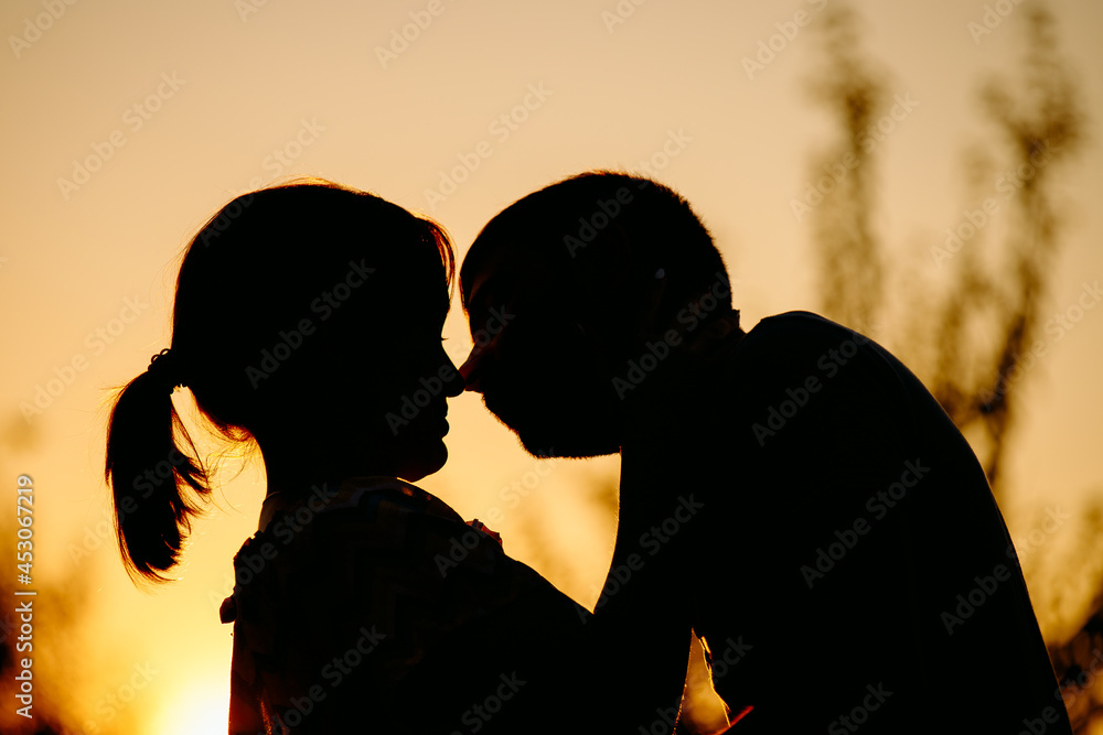 Side view portrait of a amazing young couple embracing and kissing against sunset outside while walking on the street.
