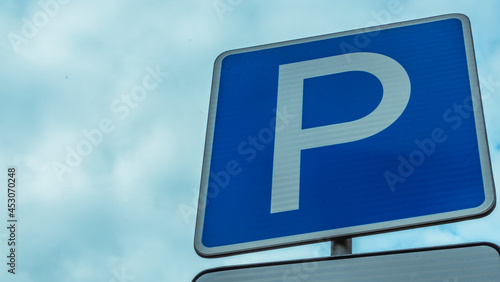 Blue road sign with letter P on rectangular plate isolated against a blue sky. Parking symbol on a cloudy blue sky background. Space for text.