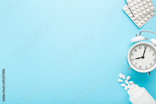 White alarm clock, plastic bottle and blister packages of pills on light blue table background. Pastel color. Closeup. Time for using medicines. Empty place for text or logo. Top down view. photo