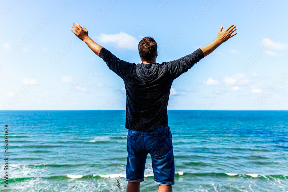 Caucasian man spreading arms,watching ocean. happy man with outstretched arms.rear view beach summer blue sky clouds Caucasian man spreading arms,watching ocean. happy man with outstretched arms.rear view beach summer blue sky clouds