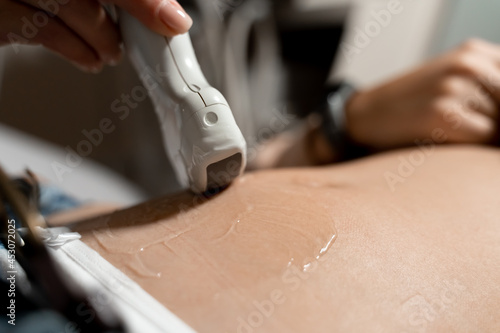 Ultrasound diagnostics of the stomach on the abdominal cavity of a girl in the clinic, close-up. The doctor holds the ultrasound probe over the patient's abdomen. Internal organs diagnostics.