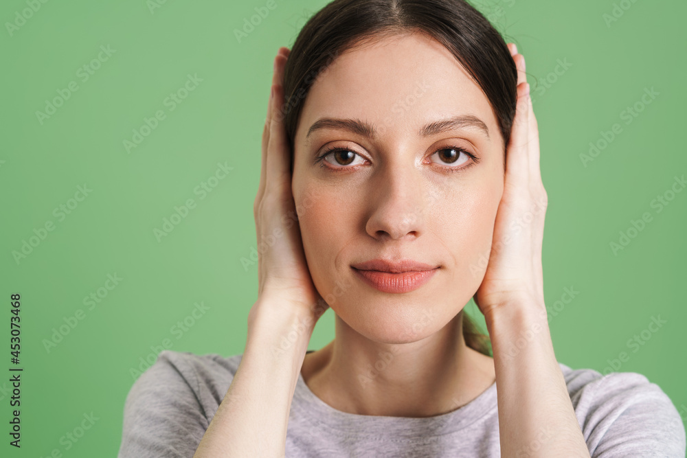 Young brunette woman covering her ears while looking at camera Young brunette woman covering her ears while looking at camera