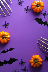 Halloween poster with festive decorations, pumpkins, spiders, skeletons hands, bats on purple background. Flat lay, top view, overhead.