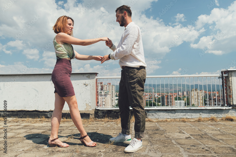Young dancing couple dance on a rooftop of a building on a sunny day.