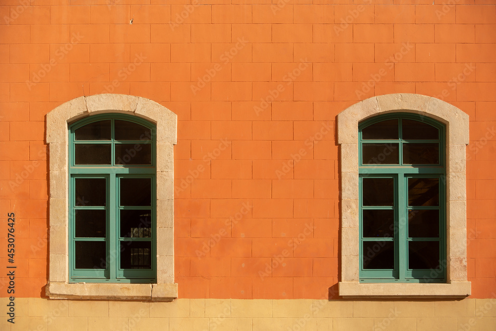 Two green timber framed windows aginst a bright orange toned exterior wall