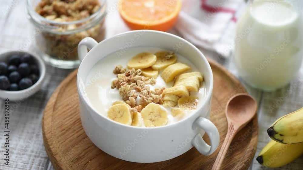 Adding granola into yogurt bowl. Greek yogurt with banana slices, crunchy oat granola topping Adding granola into yogurt bowl. Greek yogurt with banana slices, crunchy oat granola topping