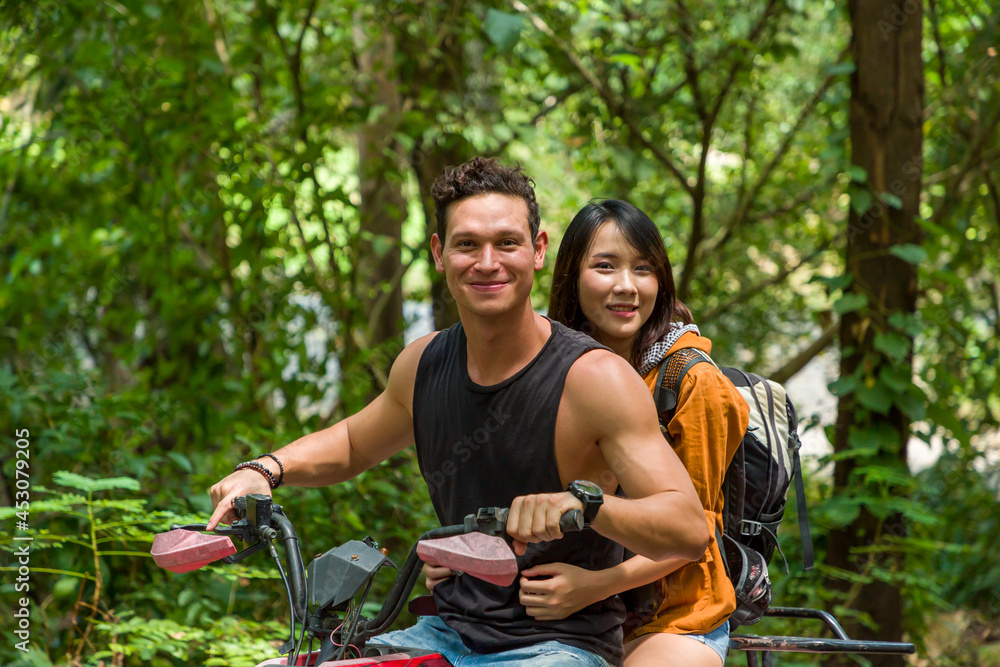 Close up of young man and woman driving off road adventure with happy and smiling. Couple riding on ATV bike or quad bike on road along forest trail on mountain. Camping, jungle adventure concept
