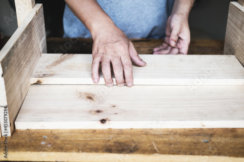 A carpenter measures the planks to assemble the parts, and build a wooden table for the customer.