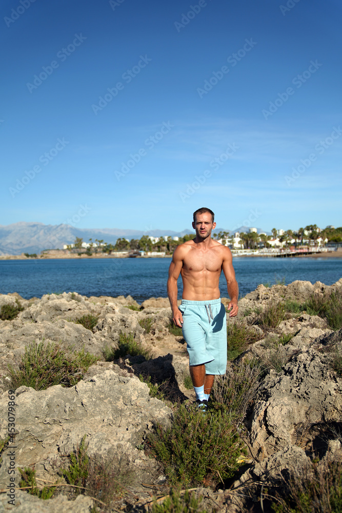 a young guy is walking along a rocky beach near the sea