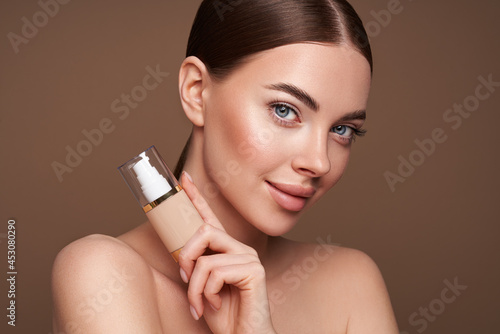 Portrait beautiful young woman with clean fresh skin. Model with foundation makeup bottle. Cosmetology, beauty and spa