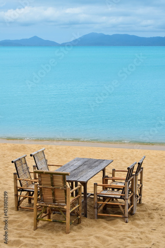 Wooden bamboo furniture  table and five chairs around on sand beach with blue sea water background in Koh Samui island  Thailand