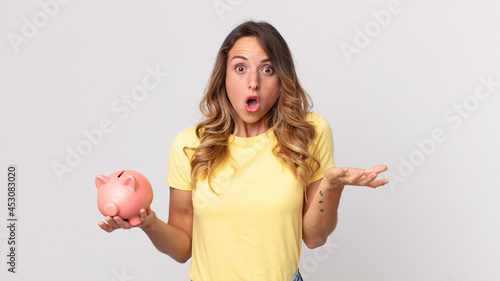 pretty thin woman amazed, shocked and astonished with an unbelievable surprise and holding a piggybank photo