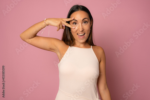 Beautiful young woman wearing casual dress smiling with happy face winking at the camera doing victory sign. number two.