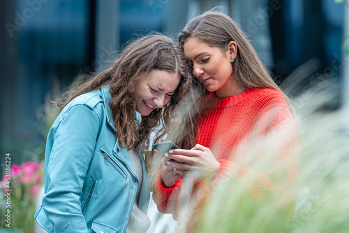 two girlfriends use a smartphone, laugh and talk, fun together, new normal tech concept photo