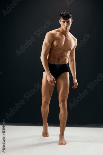 athletic man with a pumped-up muscular body in black shorts dark background