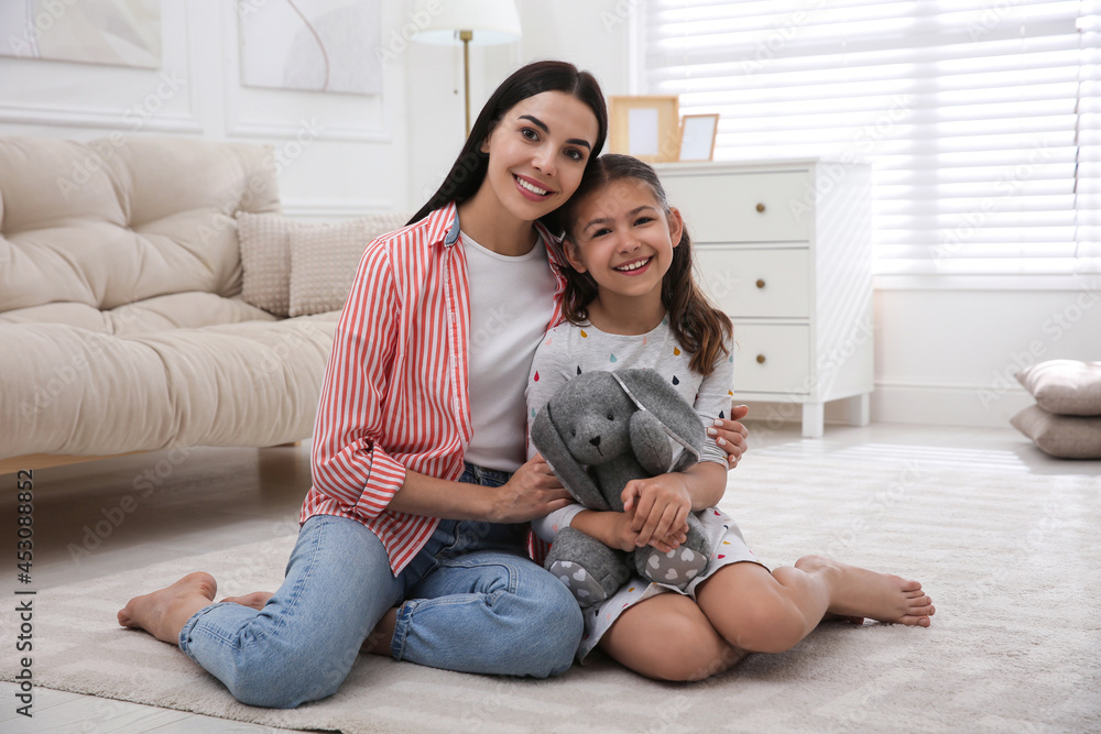 Portrait of happy young mother and her daughter on floor in living room. Adoption concept