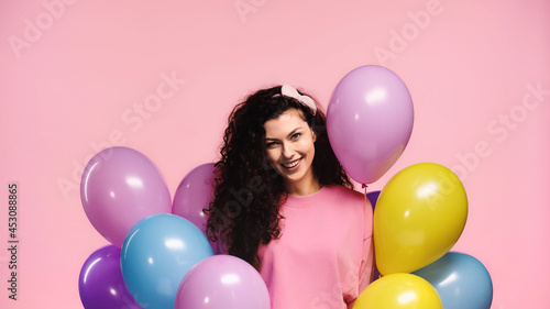 cheerful woman with colorful balloons looking at camera isolated on pink © LIGHTFIELD STUDIOS