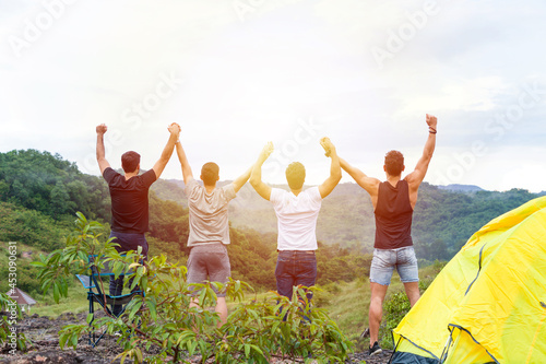 Group of male hiking and camping. Back view of group of young tourists man camping standing raising up his hands on mountain