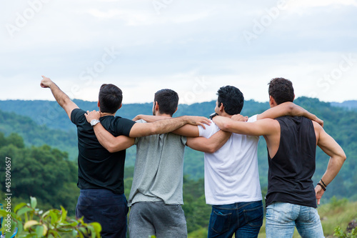 Group of male hiking and camping. Back view of group of young tourists man camping standing hugging on shoulder together and raising up his hands on mountain
