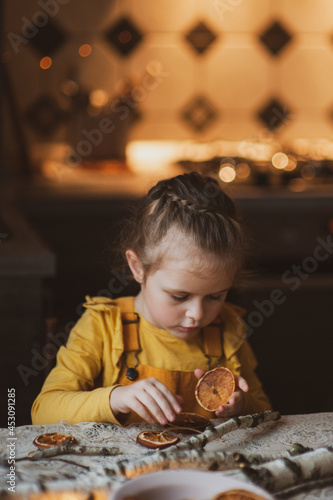 A cute sweet girl makes Christmas decorations from dried oranges  twigs and cones. Crafts for the holiday