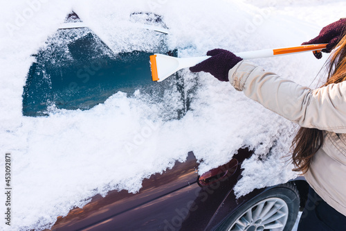 Woman cleans snow from car windows with a scraper