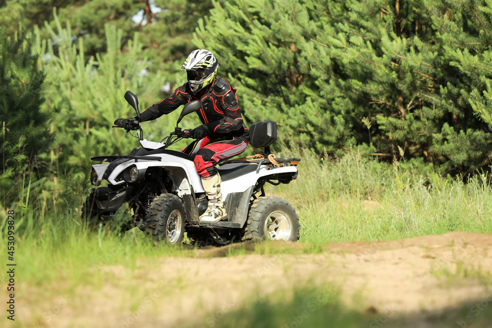 Man driving modern quad bike on sandy road near forest. Extreme sport Man driving modern quad bike on sandy road near forest. Extreme sport