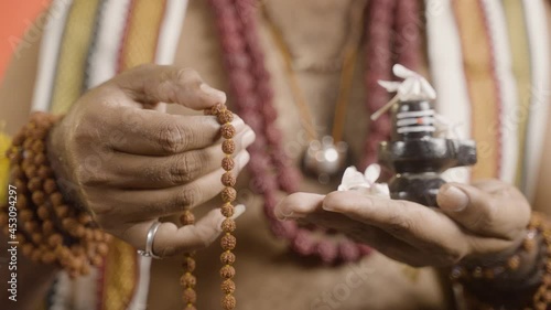 Close up hands of Indian priest meditating or chanting using rudrakshi japa mala with shiva linga in hand during navratri. photo