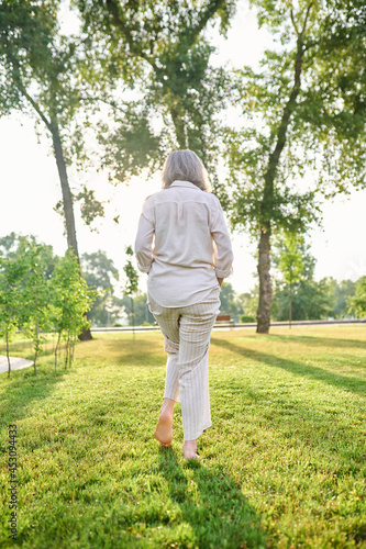 Back view of woman walking barefoot on lawn