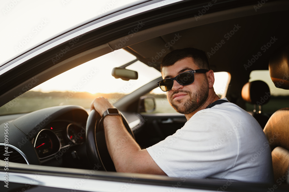 Naklejka premium Bearded man driver in sunglasses sitting in his car and looking at camera