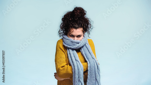 frozen woman hiding face in warm scarf isolated on blue