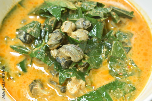 spicy boiled cockle with acacia and basil leaf in red curry coconut milk soup in bowl photo