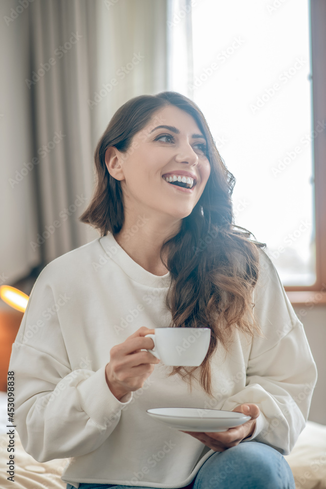 Pretty young woman sitting on the bed and drinking coffee Pretty young woman sitting on the bed and drinking coffee